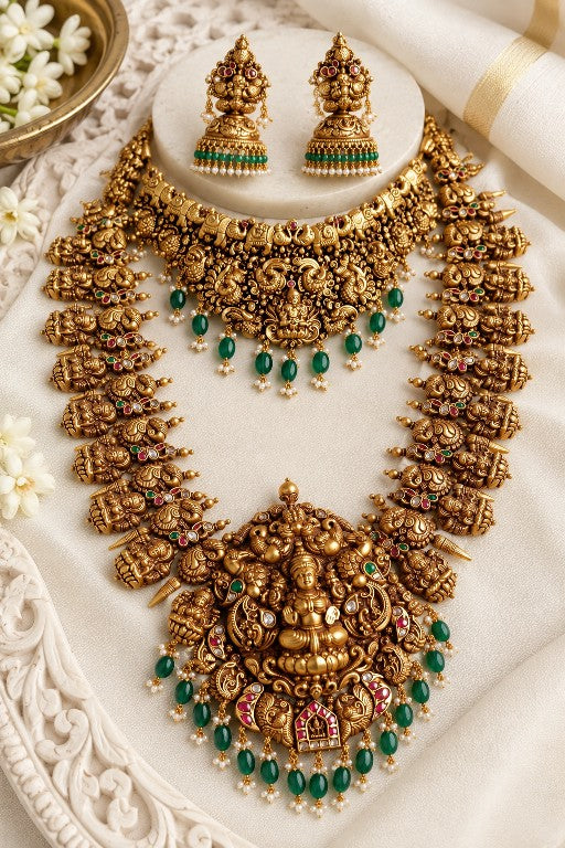 South Indian bridal jewellery set featuring traditional temple-style necklace, long haaram and matching earrings with intricate gold-tone detailing and green stone accents.