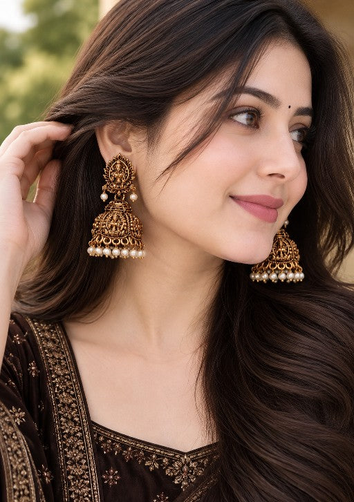 Black and gold Lakshmi jhumka earrings with white pearl drops worn by a woman in ethnic attire