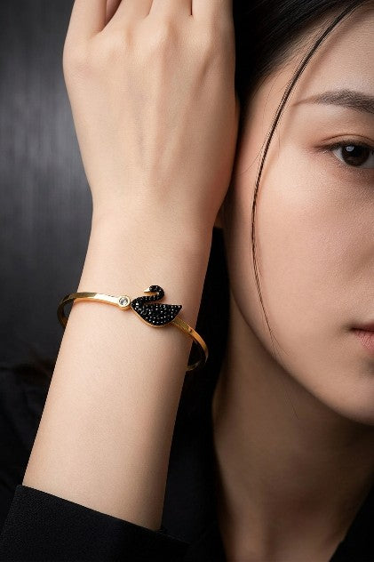 Close-up of woman wearing Tavisi Celina Swan Bracelet featuring black and white AD stones, 22K gold plated anti-tarnish waterproof bracelet for women.
