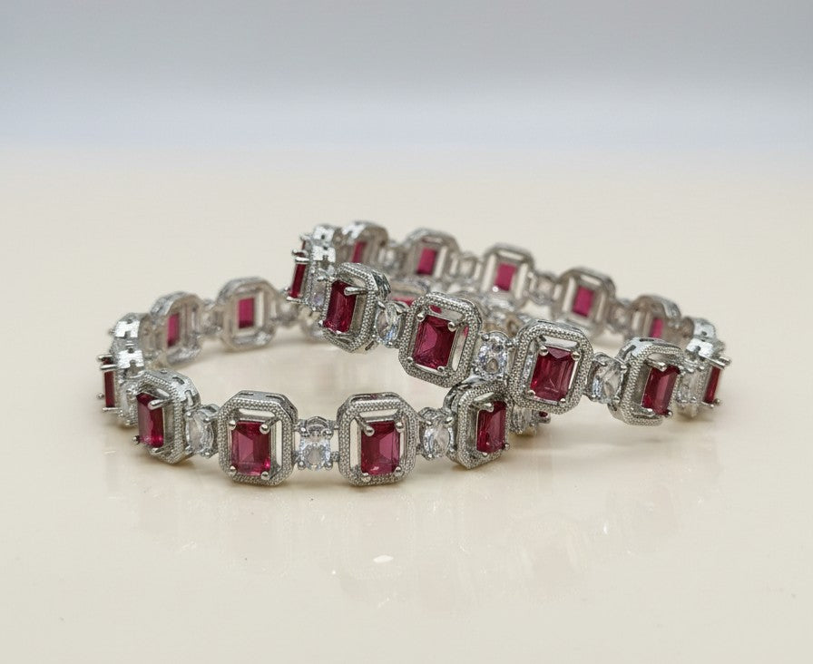 Tavisi Regal Spark CZ Silver Polish Bangles with white CZ stones and Ruby Red & Emerald Green AD stones displayed on a premium jewellery stand, available in sizes 2.6 and 2.8.